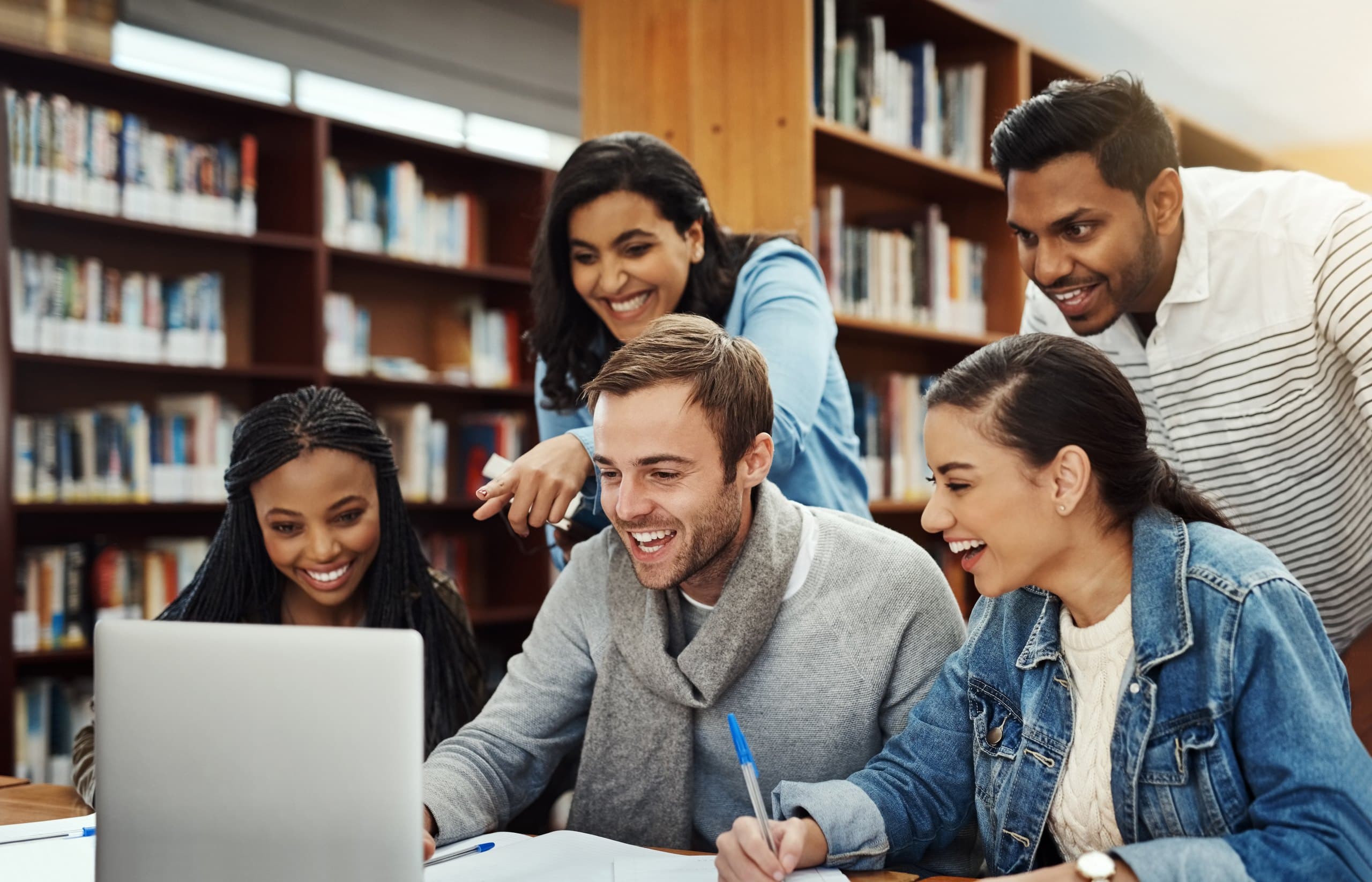 Group of students laughing over a laptop in a library