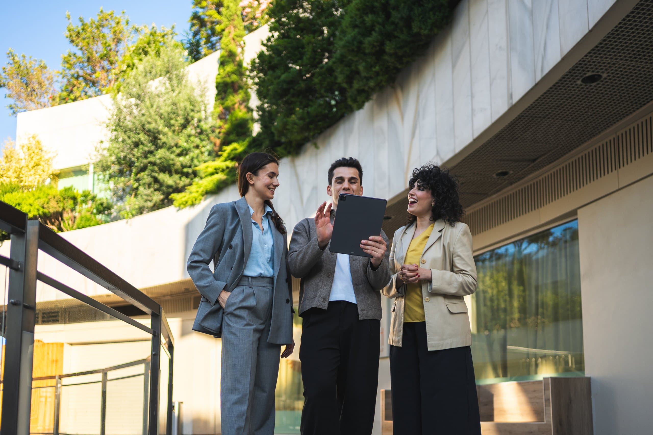 Three colleagues talking over a tablet outside a campus building